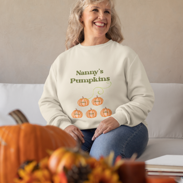 Smiling grandmother modeling custom Mama’s Pumpkins sweatshirt cream pullover with pumpkin design on couch