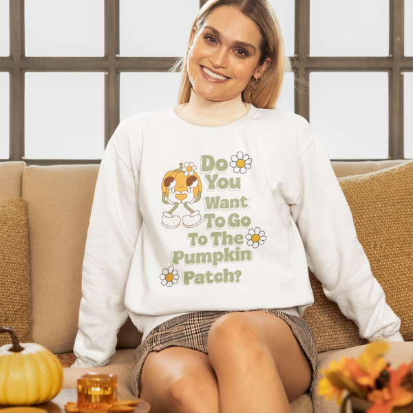 Smiling woman on couch wearing white Pumpkin Patch sweatshirt with retro pumpkin graphic and fall decor