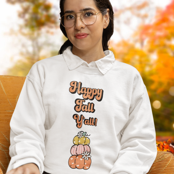 Woman wearing white Happy Fall Y’all sweatshirt with stacked pumpkins and flowers on a cozy autumn background