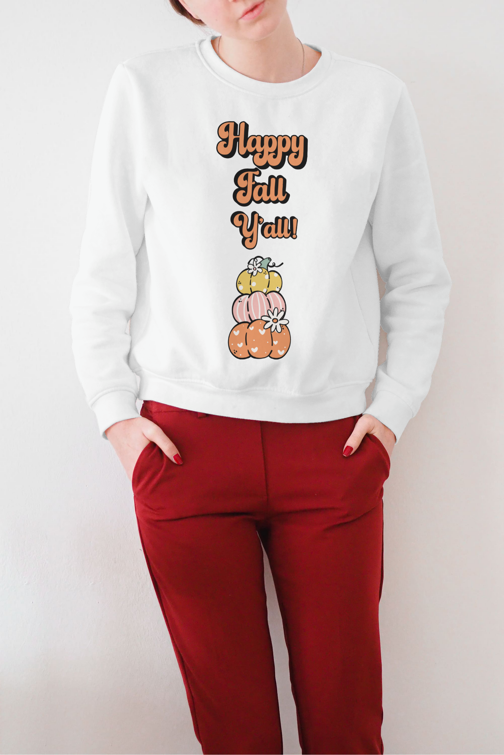 Woman wearing white crewneck Happy Fall Y’all sweatshirt with stacked pumpkins graphic paired with red pants