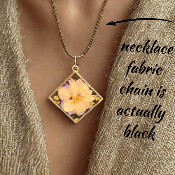 Square gold frame double-sided resin pendant with pressed pale pink flower on bronze chain over beige knit top