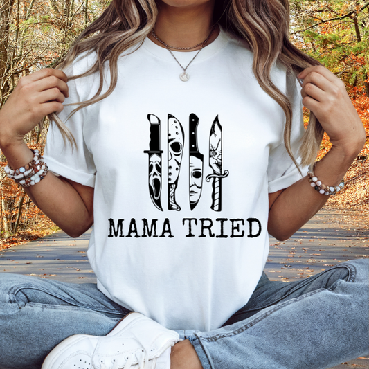 Woman wearing a white Mama Tired horror movie shirt featuring three horror knife graphics and MAMA TRIED text